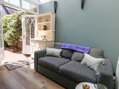 A gray sofa with pillows and a purple blanket in a room with a white cabinet next to an open door leading to a garden at Leos Place in Weymouth