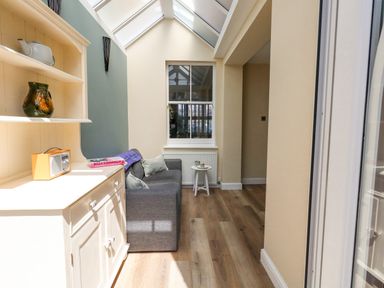 A narrow sitting area with a gray sofa, a white side table, a white cabinet with shelves, and a window at Leos Place in Weymouth
