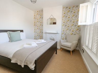 A bedroom with a bed with folded towels an armchair a mirror above a fireplace and floral wallpaper at Leos Place in Weymouth