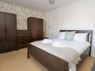 A bedroom with a double bed with towels on it two wardrobes drawers and a floral wallpaper at Leos Place in Weymouth