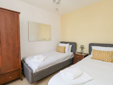 A bedroom with two single beds a wooden wardrobe a nightstand with a lamp and glasses at Leos Place in Weymouth
