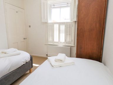A bedroom with two single beds with white linens and towels a wooden wardrobe and a window with shutters at Leos Place in Weymouth