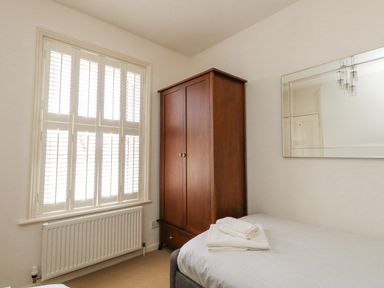 A bedroom with a bed and folded towels a wooden wardrobe and a window with shutters at Leos Place in Weymouth