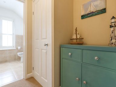 A hallway with a closed white door a green cabinet with sailboat and lighthouse decorations and a bathroom with a toilet and window in the background at Leos Place in Weymouth