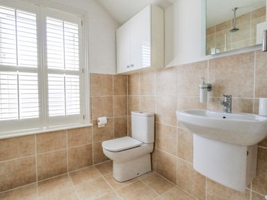 A bathroom with a toilet sink mirror wall cabinet and window shutters at Leos Place in Weymouth