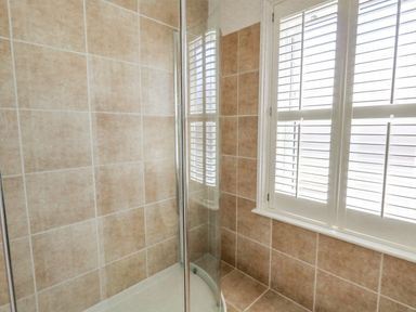 A shower area with beige tiles and a window with white shutters at Leos Place in Weymouth