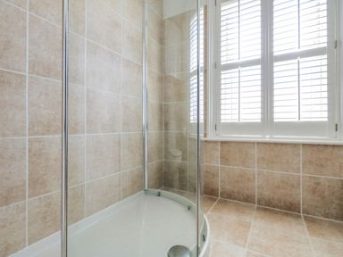 A shower enclosure with glass doors and tiled walls near a window with white blinds at Leos Place in Weymouth