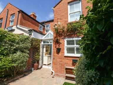 The exterior of a brick house with a small paved yard and plants around the entrance at Leos Place in Weymouth