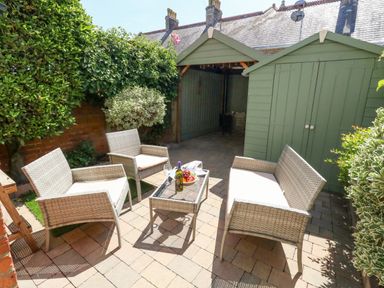 A patio with outdoor wicker furniture and green garden sheds at Leo's Place in Weymouth