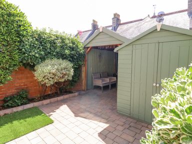 A garden with a paved patio area green shed and seating under a covered area at Leos Place in Weymouth