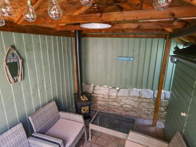 An outdoor seating area with wicker chairs a glass table a wood stove and wooden walls at Leos Place in Weymouth