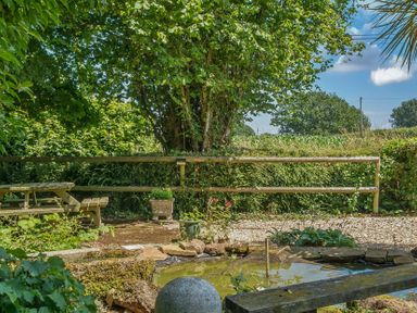 A garden with a table and benches near a pond at 2 Pigsfoot Cottages Ash Thomas near Halberton, Devon