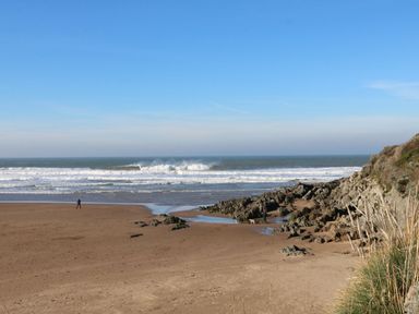 A beach with waves and a person walking at 2 Pigsfoot Cottages in Ash Thomas near Halberton, Devon