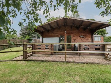 A wooden cabin with a fenced porch and garden at Pigsfoot Lodge in Ash Thomas near Halberton Devon