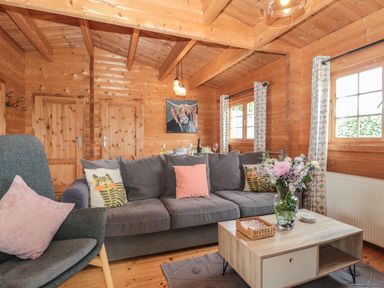 A wooden living room with a gray sofa and armchair a coffee table with flowers and a painting on the wall at Pigsfoot Lodge in Ash Thomas near Halberton Devon