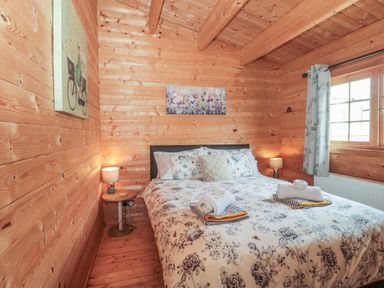 A bedroom with a bed a floral duvet two bedside tables with lamps and a window with curtains at Pigsfoot Lodge in Ash Thomas near Halberton Devon