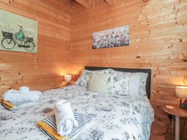 A bedroom with a bed with floral bedding two bedside tables with lamps and wooden walls at Pigsfoot Lodge in Ash Thomas near Halberton Devon