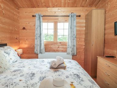 A wooden bedroom with a bed folded towels a window with curtains a wardrobe and a chest of drawers at Pigsfoot Lodge Ash Thomas near Halberton Devon