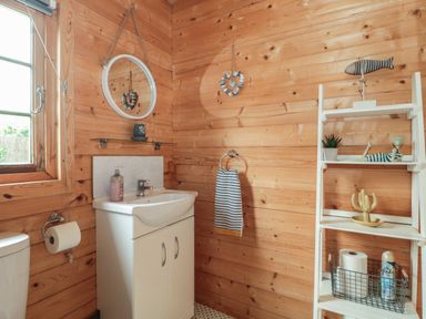A bathroom with wooden walls a white sink a mirror a towel rack and a white shelf with decorations at Pigsfoot Lodge in Ash Thomas near Halberton Devon