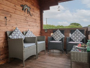 A covered wooden porch with four wicker chairs with patterned cushions and a small glass-topped table at Pigsfoot Lodge in Ash Thomas near Halberton Devon