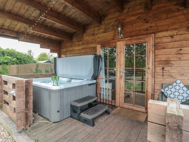 A porch area with a hot tub steps glass doors and wooden walls at Pigsfoot Lodge in Ash Thomas near Halberton Devon