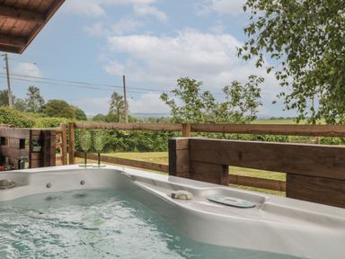 An outdoor hot tub with two green glasses on the edge overlooking a wooden fence and trees at Pigsfoot Lodge Ash Thomas near Halberton Devon