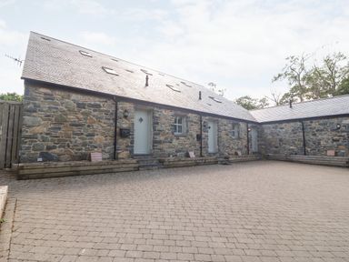 A stone building with multiple doors and windows and a paved courtyard at 3 Pensyflog Barns in Porthmadog