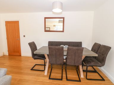 A dining room with a rectangular table, six chairs, a wall mirror, and a wooden door at 3 Pensyflog Barns Porthmadog