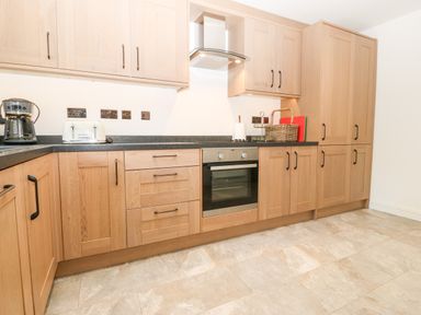 A kitchen with wooden cabinets black countertop oven coffee maker toaster and a basket on the counter at 3 Pensyflog Barns in Porthmadog