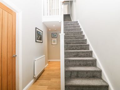 A hallway with wooden floor and a carpeted staircase next to a wooden door at 3 Pensyflog Barns in Porthmadog