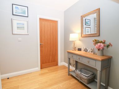 A hallway with a wooden door a gray console table with a lamp flowers a decorative home sign and a mirror at 3 Pensyflog Barns in Porthmadog