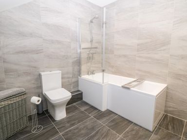 A bathroom with a toilet and a bathtub with shower at 3 Pensyflog Barns in Porthmadog