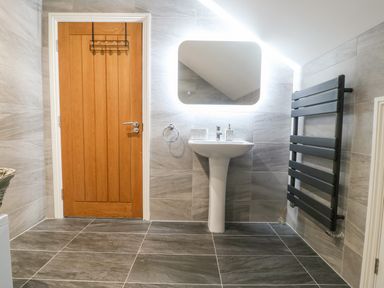 A bathroom with a wooden door a pedestal sink a lighted mirror and a black towel radiator at 3 Pensyflog Barns in Porthmadog
