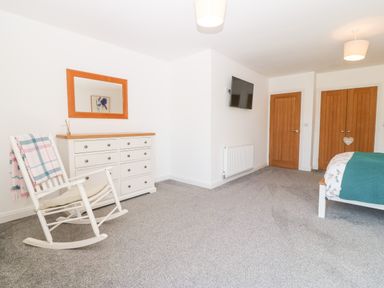 A bedroom with a rocking chair dresser mirror wall-mounted TV bed and wardrobe at 3 Pensyflog Barns in Porthmadog
