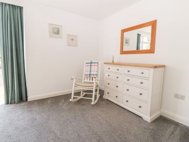 A room with a white rocking chair and a white dresser with a mirror above it at 3 Pensyflog Barns in Porthmadog