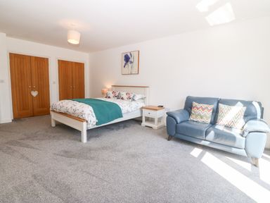 A bedroom with a bed a nightstand a blue sofa and two wooden closet doors at 3 Pensyflog Barns in Porthmadog