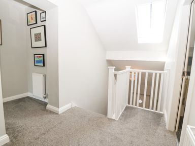 A carpeted hallway with white walls and a white railing by the stairs with framed pictures on the wall at 3 Pensyflog Barns in Porthmadog