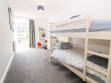 A bedroom with a bunk bed toys a chest of drawers and a window with curtains at 3 Pensyflog Barns in Porthmadog