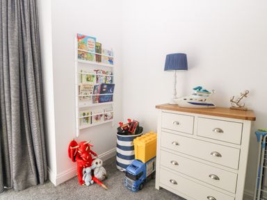 A child's corner with a white dresser topped with a blue lamp toy boat and anchor beside a toy storage bin stuffed animals and a wall-mounted book rack at 3 Pensyflog Barns in Porthmadog