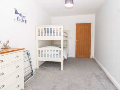 A bedroom with a bunk bed a wooden door a dresser and a drying rack at 3 Pensyflog Barns in Porthmadog