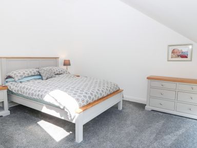 A bedroom with a bed a bedside table with a lamp a dresser and a framed photo on the wall at 3 Pensyflog Barns in Porthmadog