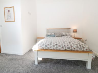 A bedroom with a bed a bedside table with a lamp and a framed artwork on the wall at 3 Pensyflog Barns in Porthmadog
