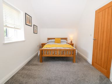 A bedroom with a wooden bed and bedside tables a lamp on one table and framed pictures on the wall at 3 Pensyflog Barns in Porthmadog
