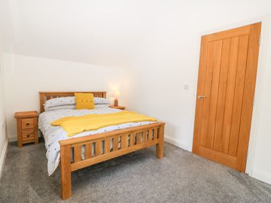 A bedroom with a wooden bed and side tables with lamp and wooden door at 3 Pensyflog Barns in Porthmadog