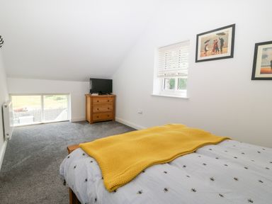 A bedroom with a bed covered with a bee patterned duvet and yellow blanket a wooden chest of drawers with a television on top and framed pictures on the wall at 3 Pensyflog Barns in Porthmadog