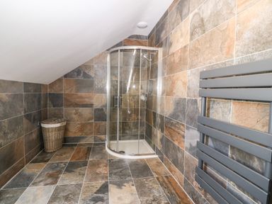 A bathroom with a curved glass shower enclosure a wicker laundry basket and a wall-mounted towel radiator at 3 Pensyflog Barns in Porthmadog