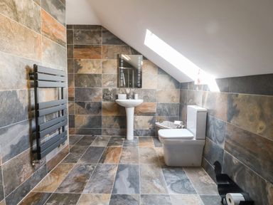 A bathroom with tiled walls and floor a pedestal sink a toilet a mirror a towel radiator and a skylight at 3 Pensyflog Barns in Porthmadog