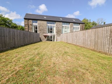 A grassy fenced backyard with a stone building and large windows at 3 Pensyflog Barns in Porthmadog