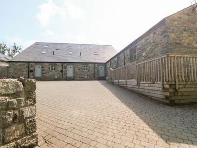 A stone building with three doors and a paved courtyard at 3 Pensyflog Barns in Porthmadog