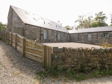 A stone barn building with multiple doors and windows surrounded by a wooden fence and a stone wall at 3 Pensyflog Barns in Porthmadog